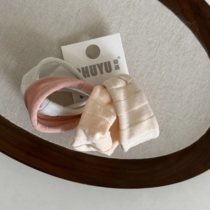 Lot de 3 chouchous élastiques côtelés en blanc, rose et beige sur un plateau en bois