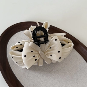 Detail view of a vintage cream fabric hair claw clip with black polka dots and silk bow design
