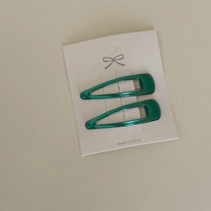 Detail view of two dark green drip oil metal BB clips on a white textured display card