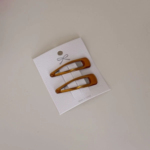 Close-up of two amber water-drop hair clips on a white card with a textured finish