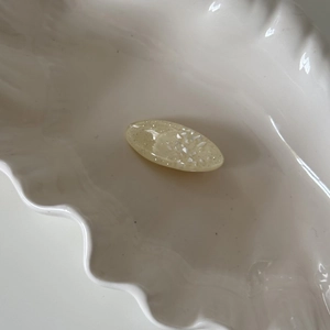 Elegant oval resin hair clip with mother-of-pearl flakes on a white ceramic dish