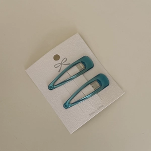 Detail of lake green teardrop-shaped BB hair clips on minimalist paper card packaging