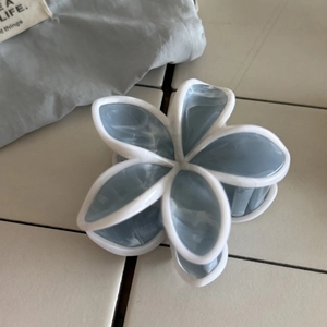 Dettaglio del fermaglio per capelli a fiore in acetato marmorizzato blu su piastrelle bianche