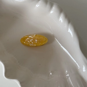 Close-up of amber yellow oval resin hair clip with white flakes and gold glitter inside