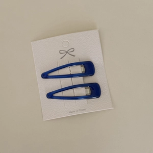 Detail of two dark blue drop-shaped BB hair clips on a white texture display card