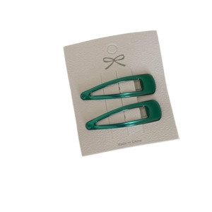 Set of two green teardrop metal snap clips for women displayed on a beige card holder
