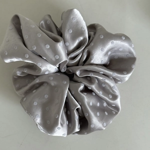 Close-up of silver-grey satin scrunchie with white polka dots and soft pleated texture