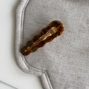 Dettaglio di un fermaglio per capelli tartarugato con clip in metallo dorato e logo