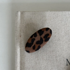 Close-up of oval leopard print hair clip with soft flocked texture on beige linen cloth