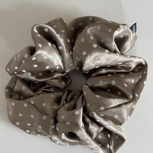 Close-up of champagne satin scrunchie with white polka dots and fashion label