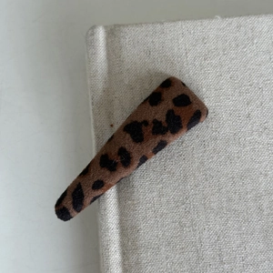 Detailed view of leopard print fabric hair clip on a vintage beige book background