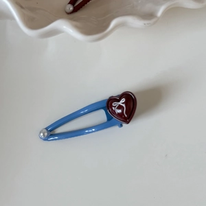 Dettaglio di fermaglio blu in metallo con perla bianca e ciondolo a cuore rosso