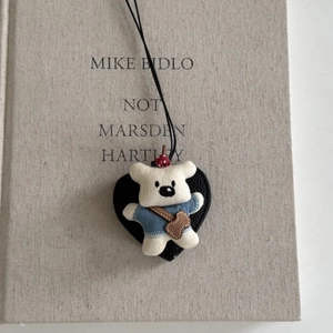 Pendentif ours tricoté blanc avec chemise bleue sur base en cuir noir en forme de cœur