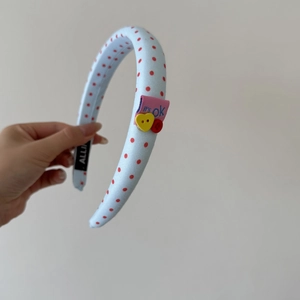 Détail du serre-tête en tissu bleu clair à pois avec boutons décoratifs et étiquette tissée