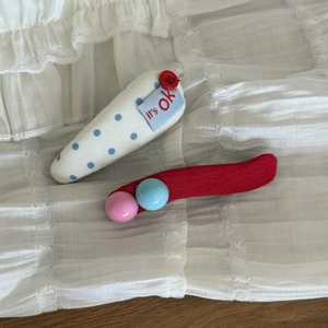 Détail d'une pince à cheveux en tissu bleu à pois et d'une barrette rouge avec perles