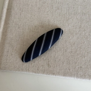Detail shot of navy blue striped fabric oval hair clip on textured beige linen background