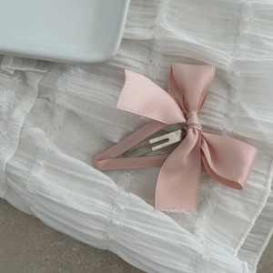 Sweet pink satin bow hair clip with silver alligator grip on soft white fabric