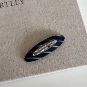 Close-up of navy blue striped fabric hair clip with a metal BB clip on textured cloth