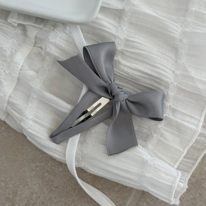 Detail of elegant grey satin bow hair clip on a minimalist white textured fabric