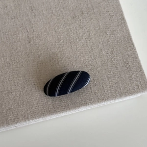 Detailed view of an oval navy striped fabric hair clip on a natural linen surface