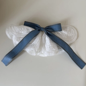 Détail macro du col en dentelle blanche orné d'un nœud en ruban de denim bleu
