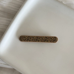 Close-up of leopard print hair clip with metallic trim on white ceramic tray