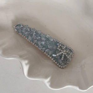 Close-up of blue crystal BB hair clip with rhinestone bow on white ceramic plate