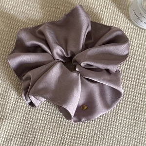 Elegant dusty pink satin scrunchie with textured edge and round gold metal logo tag