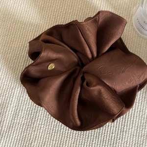 Detail of dark brown satin scrunchie with golden metal charm on a soft knitted background