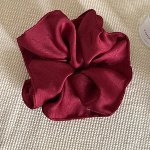 Detailed texture of burgundy satin scrunchie showing glossy fabric folds and soft sheen