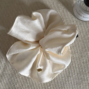 Detailed close-up of cream silk satin scrunchie with elegant golden oval logo plaque