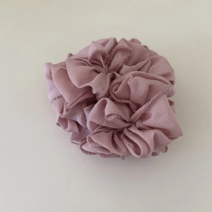 Dettaglio di scrunchie in chiffon a pieghe rosa chiaro con petali a strati su sfondo beige