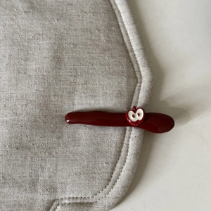 Detailed close-up of dark red hair clip with cute apple accent on a beige linen fabric