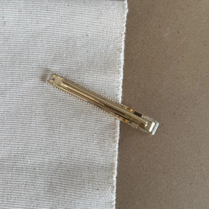 Detail shot of golden metal alligator hair clip with Handmade engraving on a textured surface