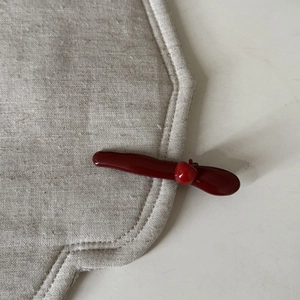 Detail of a dark red apple charm hair clip on a beige fabric edge with a glossy finish