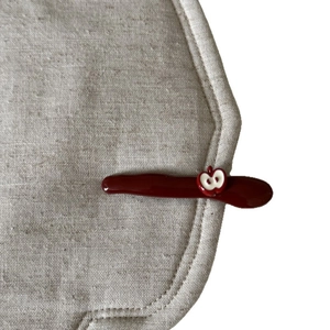 Deep red apple hair clip with glossy resin finish on beige linen fabric background