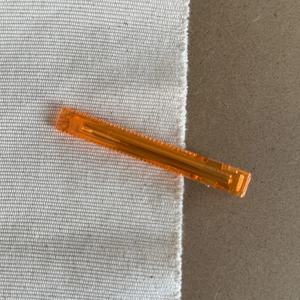 Detail of a rectangular translucent orange hair clip with a fine non-slip edge texture