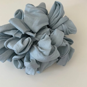 Dettaglio di uno scrunchie plissettato oversize blu-grigio con trama di tessuto a strati