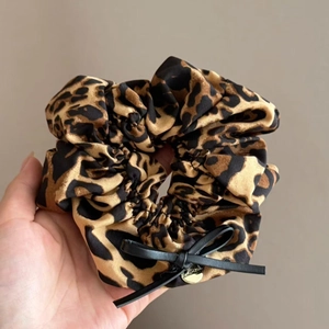 Détail d'un chouchou léopard avec un nœud en ruban noir et un pendentif en métal doré