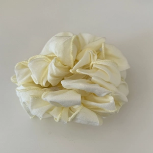 Dettaglio dell'elastico per capelli in raso crema plissettato con cuciture fini e trama