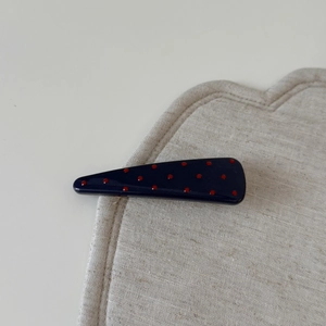 Détail macro de la pince à cheveux bleu marine à pois rouges sur un tapis de texture beige