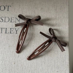 Detail view of retro brown plaid bow hair clips with white stitching on snap metal base