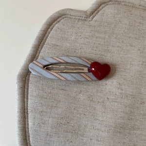 Dettaglio molletta per capelli a righe blu con cuore rosso 3D su sfondo di lino
