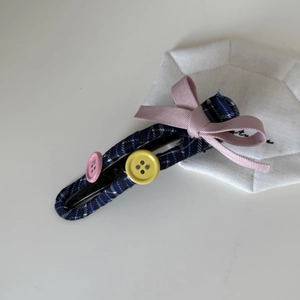Close-up of blue checkered fabric hair clip with pink ribbon bow and buttons