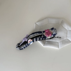 Detailed view of blue striped fabric hair clip with purple bow and pink bear accessory