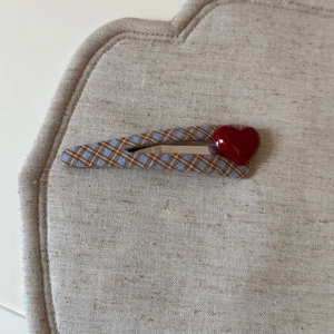 Fermaglio per capelli a quadretti blu e marroni con cuore rosso 3D su fondo beige