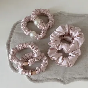 Pink satin hair scrunchies set with white pearls and beads on a textured grey mat