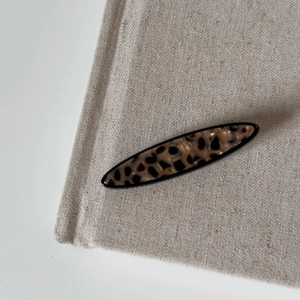Details der ovalen Haarspange mit Leopardenmuster auf beigem Stoff und schwarzem Rand