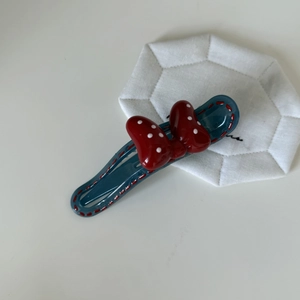 Detail view of blue resin hair clip with red polka dot bow and stitch texture accents