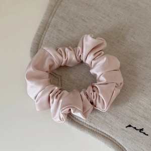 Pink satin scrunchie with pearl luster and soft pleats shown in a 45-degree top view